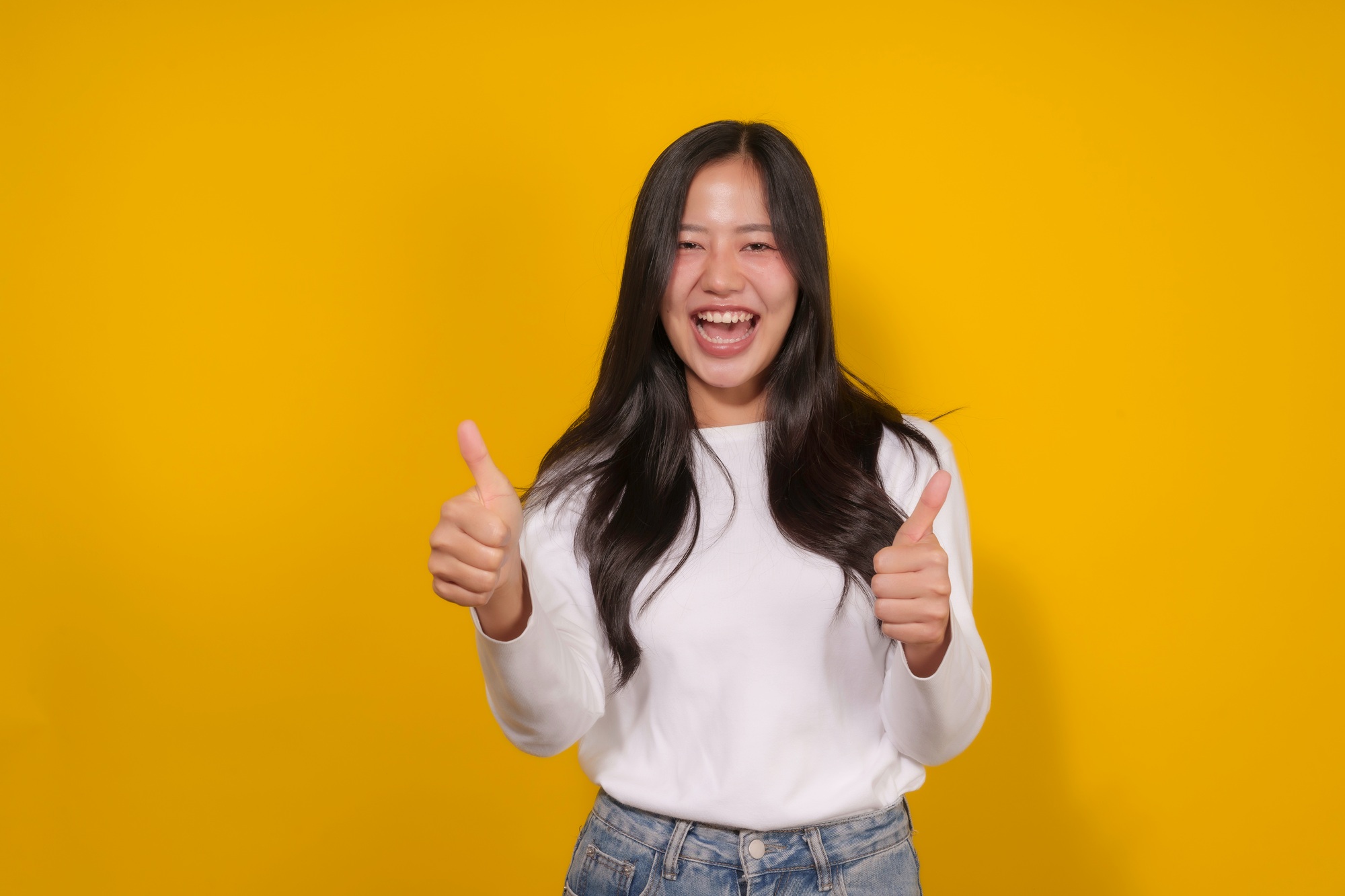 Young woman stands in front of a cheerful yellow background, smiling brightly